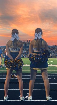 two cheerleaders standing on the sidelines at a football game