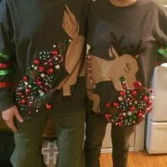 two people standing next to each other in front of a christmas tree and reindeer sweater