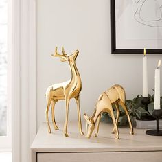 two gold deer figurines sitting on top of a table next to a candle