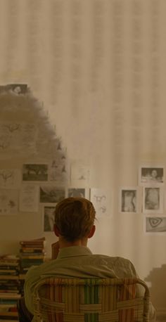 a man sitting in a chair with his back to the camera and looking at pictures on the wall behind him