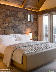 a bedroom with stone walls and white linens on the bed, along with a large window