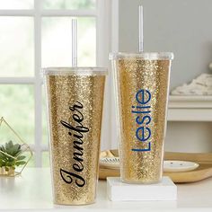 two gold glitter tumblers with straws on the side, one that says leavee