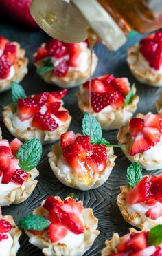 strawberries and cream tarts are being drizzled with syrup from a bottle