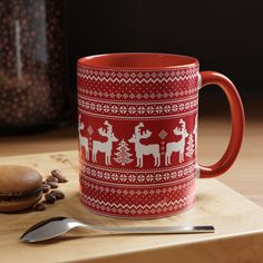 a red and white coffee mug sitting on top of a wooden table next to a spoon