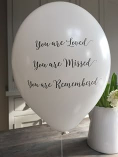 a white balloon with the words you are loved on it next to a flower vase