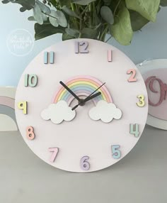 a pink clock with rainbows and clouds on the face next to a potted plant