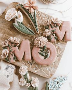 the word mom spelled out with flowers and leaves on a cutting board next to some cookies