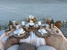 the table is set with candles, plates and napkins for dinner on the beach