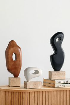 three modern sculptures on wooden blocks in front of a white wall and bookshelf