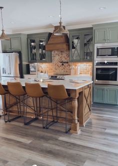 a kitchen with an island and chairs in the center, surrounded by green cabinetry