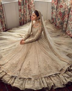 a woman sitting on top of a bed wearing a wedding dress with long sleeves and veil