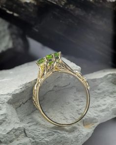 a yellow gold ring with a green stone in the center on top of some rocks