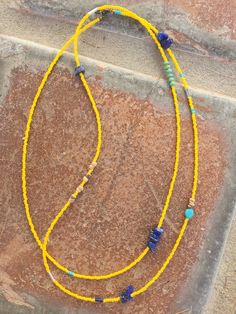 a yellow beaded necklace with blue and green beads is on the ground next to a brick wall