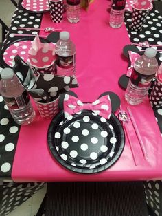 a minnie mouse themed table setting with pink and black polka dot paper plates, water bottles, and napkins