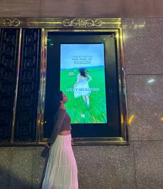 a woman standing in front of a large screen with a movie on it's wall