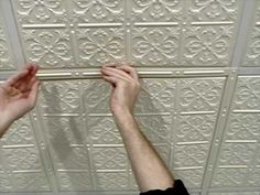 two hands are reaching up to the ceiling tiles that have been decorated with white flowers