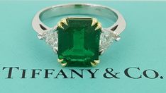 an emerald and diamond ring sitting on top of a blue box