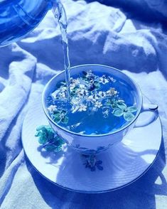 blue liquid being poured into a bowl filled with flowers on a saucer and plate