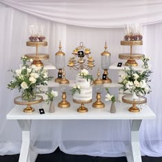 a white table topped with lots of cakes and desserts covered in gold trimming