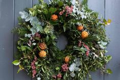 a wreath hanging on the side of a door with oranges and greenery around it