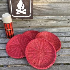 three red wicker baskets sitting on top of a wooden bench next to a bottle