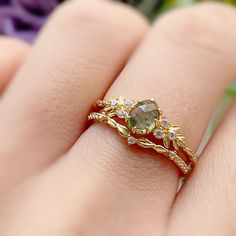 a close up of a person's hand with a ring on their finger and flowers in the background