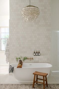 a white bath tub sitting under a chandelier next to a wooden foot stool