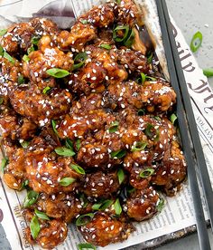 a tray filled with chicken covered in sesame seeds and seasoning on top of newspaper