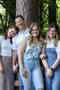 a group of people standing next to each other in front of a tree with their arms around one another