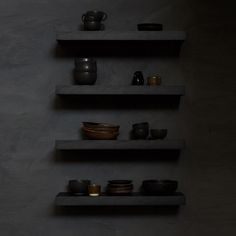 three shelves with bowls, cups and plates on them in a dark room by the wall