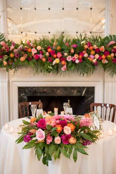 a table with flowers and candles on it in front of a fire place decorated with greenery