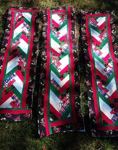 three quilts laid out on the grass with red, green and white ribbons hanging from them