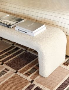 a white bench with two books on it and a couch in the back ground behind it