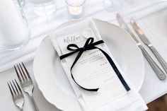 a white plate with a black ribbon on it and silverware next to the place setting