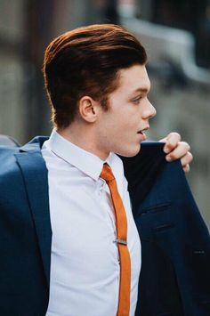 a man in a suit and orange tie is holding his jacket up to his chest