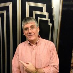 a man is standing in front of some black and gold art deco style doors with his finger pointing at the camera