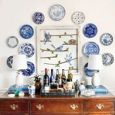 blue and white plates hang on the wall above a table with wine bottles, glasses, and vases