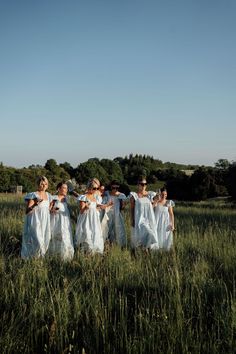 a group of women in white dresses standing in tall grass with trees in the background