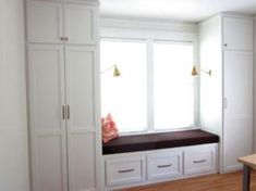 a window seat in the corner of a room with white cabinets and drawers on either side