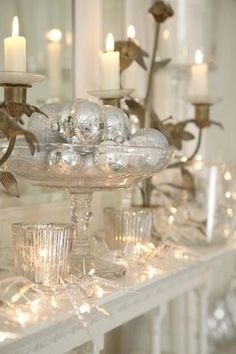 a white table topped with lots of glass vases filled with christmas ornaments and lights