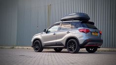 the rear end of a silver suv with luggage on it's roof, parked in front of a building