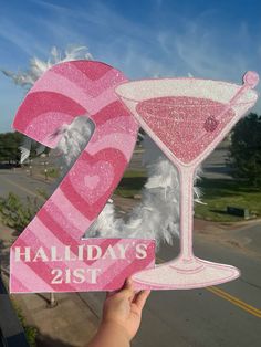 a hand holding up a pink 21st birthday sign with a martini in the shape of a number