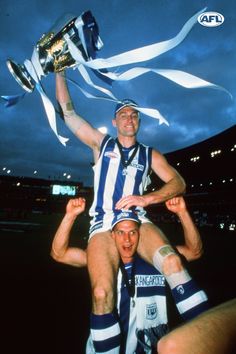 a man holding up a trophy while standing next to another man on top of him