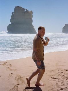 a man is walking on the beach with a cup in his hand