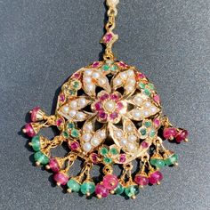 This magnificent mang teeka / tikka is designed in 22k gold with an intricately placed ruby, emerald and pearl design. Its chain measures 4 inches in length with a detachable hook at the end. It boasts an impressive total weight of 8.39 gms, 0.85 gms of which is concentrated in the ruby-emerald beads. This timeless piece is the perfect accessory for special occasions and can be passed down for generations as a treasured heirloom. The blend of precious gems and gold make it a stunning piece sure Temple Jewelry Round Cutdana Tikka, 22k Gold Temple Jewelry Tikka, Gold Cutdana Tikka Temple Jewelry, Mang Tikka Gold Antique, Green Meenakari Tikka Temple Jewelry, 22k Gold Jewelry Necklaces, 22k Gold Jewelry, Pearl Necklace Set, Emerald Bead