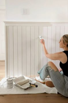 a woman is sitting on the floor with paint and rollers in her hand as she paints the wall