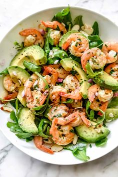 a white bowl filled with shrimp, avocado and spinach salad on top of a marble table