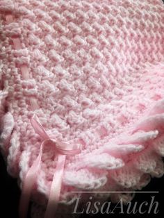 a pink crocheted baby blanket on top of a black surface