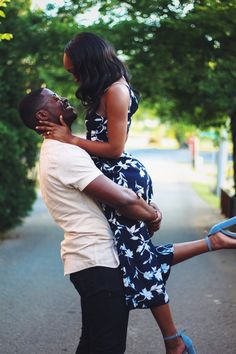 a man holding a woman in his arms while walking down the street with trees behind him