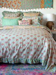 a bed with lots of pillows on top of it and a colorful wall hanging above it